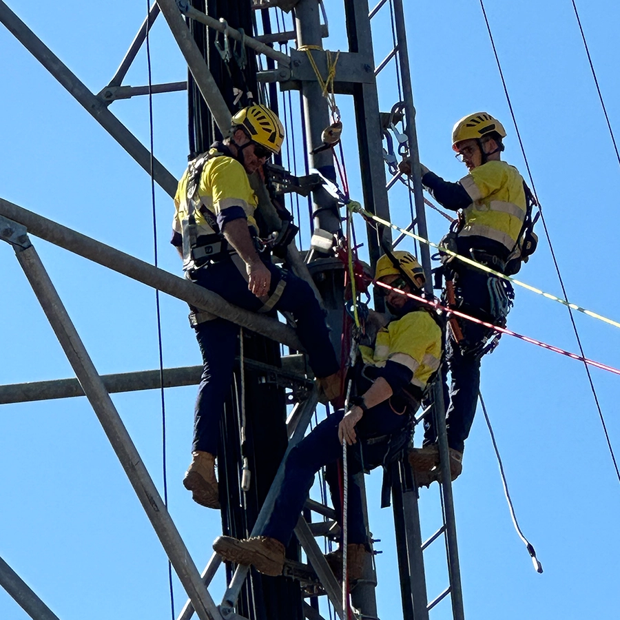 Three workers in safety gear performing maintenance on a metal communication tower.