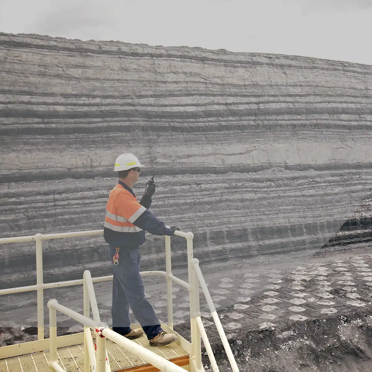 Mine site operator overlooks an open mine while using a two-way radio to contact their team.