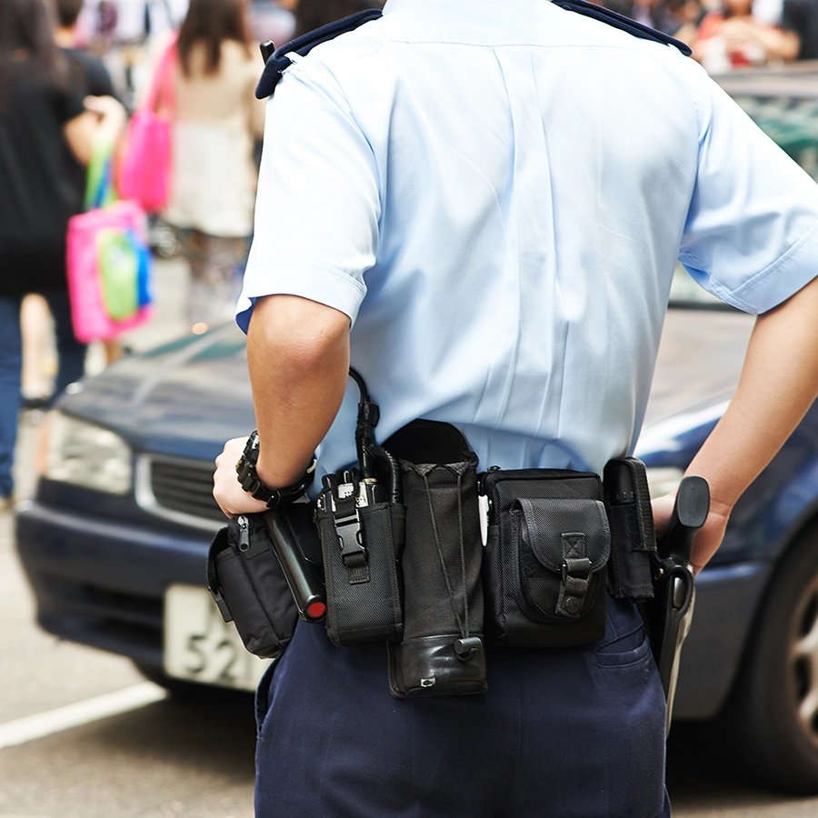 Police officer with a belt-mounted P25 two-way radio standing in a public area.