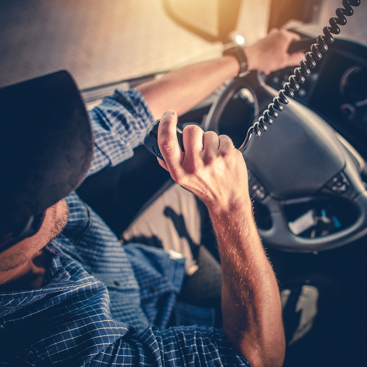 Driver using a CB radio microphone inside a vehicle, with the radio unit mounted on the dashboard.