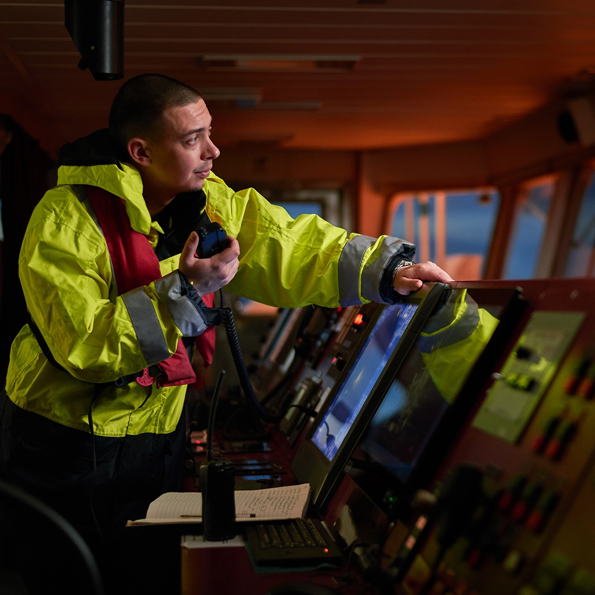 Ship operator using a handheld two-way radio and digital controls on the bridge, representing IntelliPort’s unified maritime data platform.