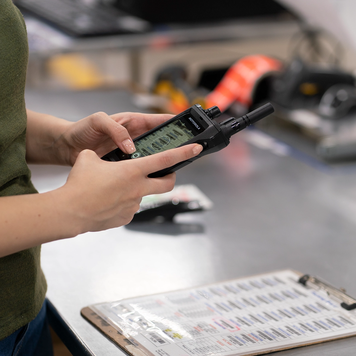 Person using a MOTOTRBO Ion smart radio at a workstation with a clipboard and office supplies in the background.