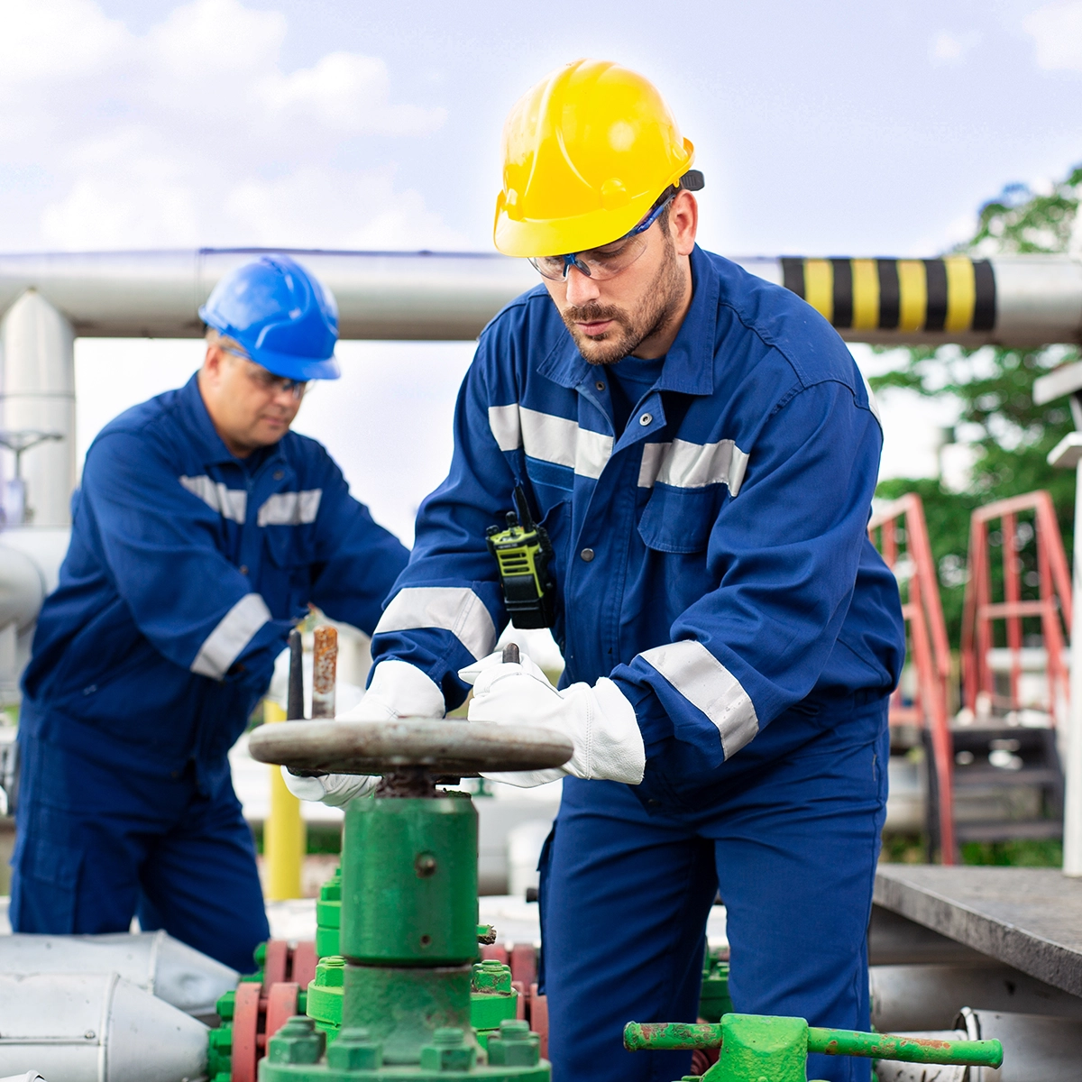 Industrial personnel adjusting valves on green piping systems, wearing safety gear and working in a structured facility.