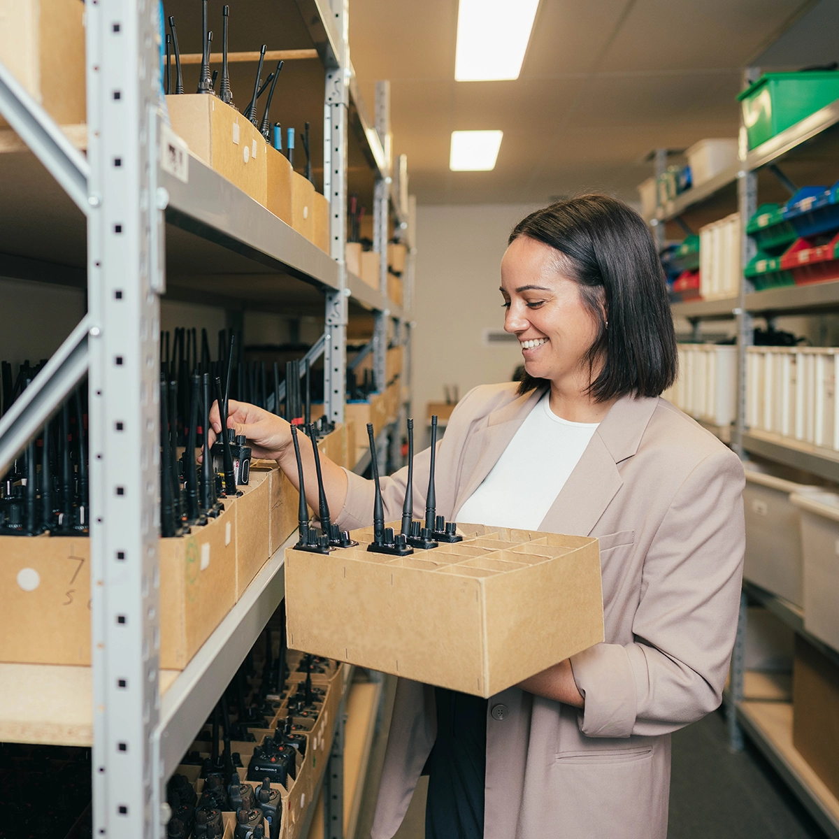 Person selecting radios from storage shelves and placing them into a cardboard box in a well-lit storeroom.