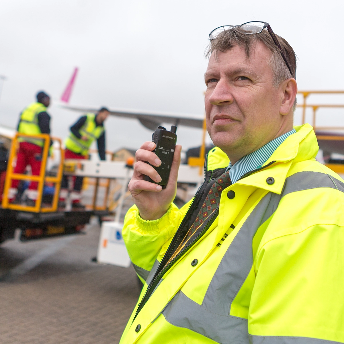 Person in high-visibility clothing holding a two-way radio on an airport tarmac.
