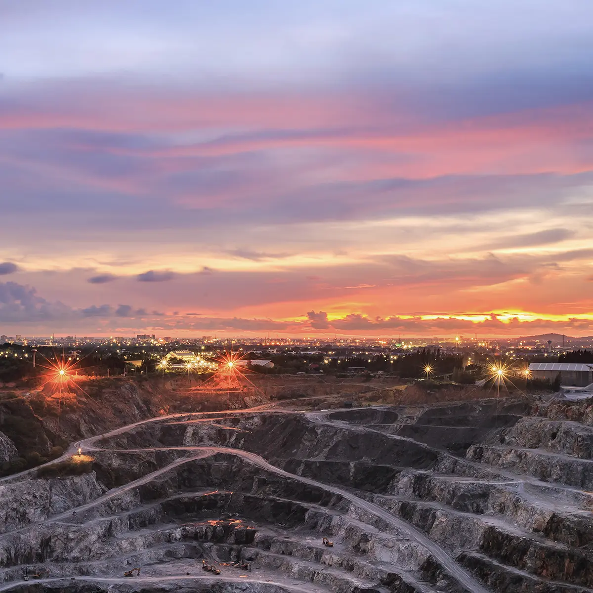 Open-pit mine at sunset with terraced levels and illuminated roads, representing remote operational environments.