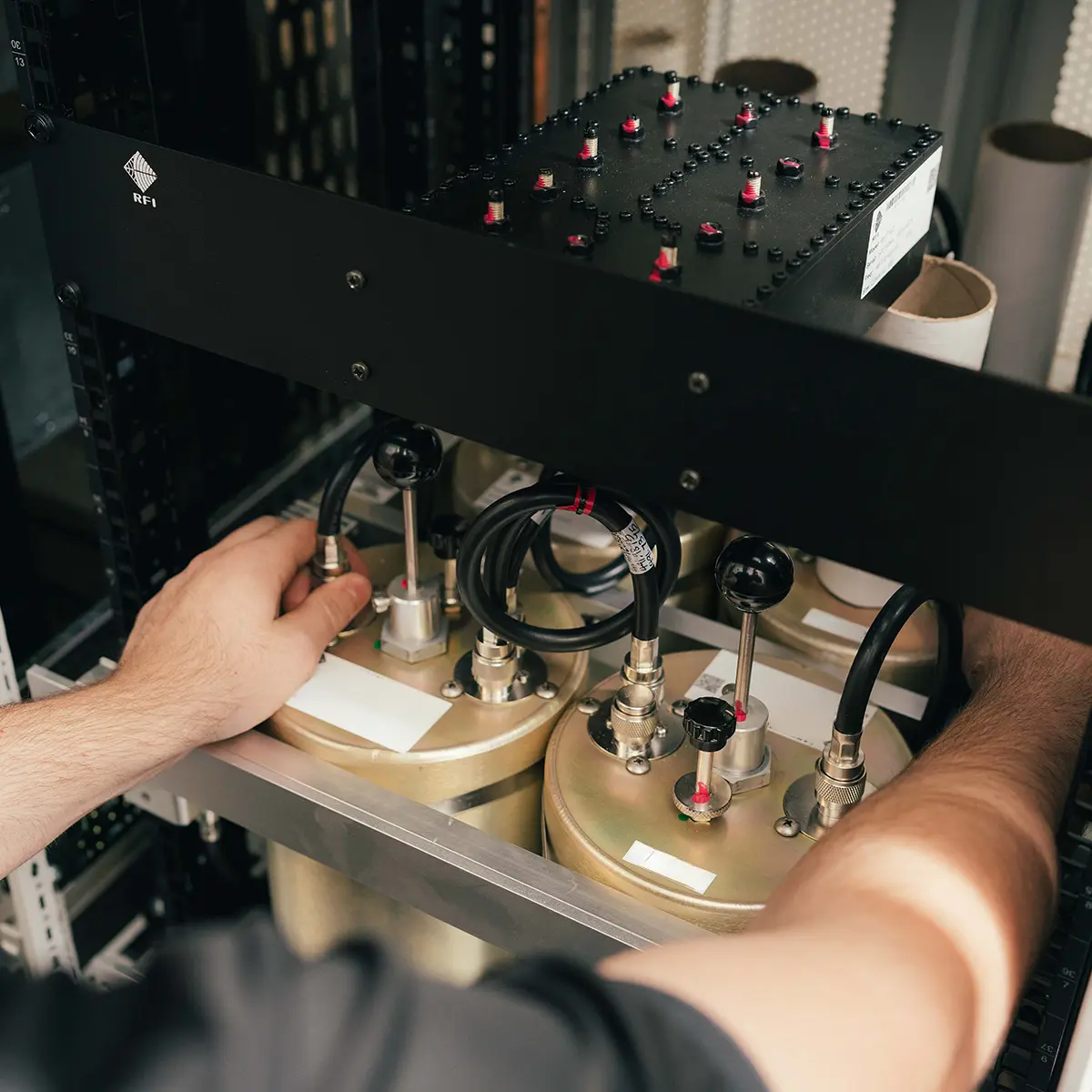 Hands of a technician working on electronic equipment within a server cabinet, featuring multiple connectors and cables.