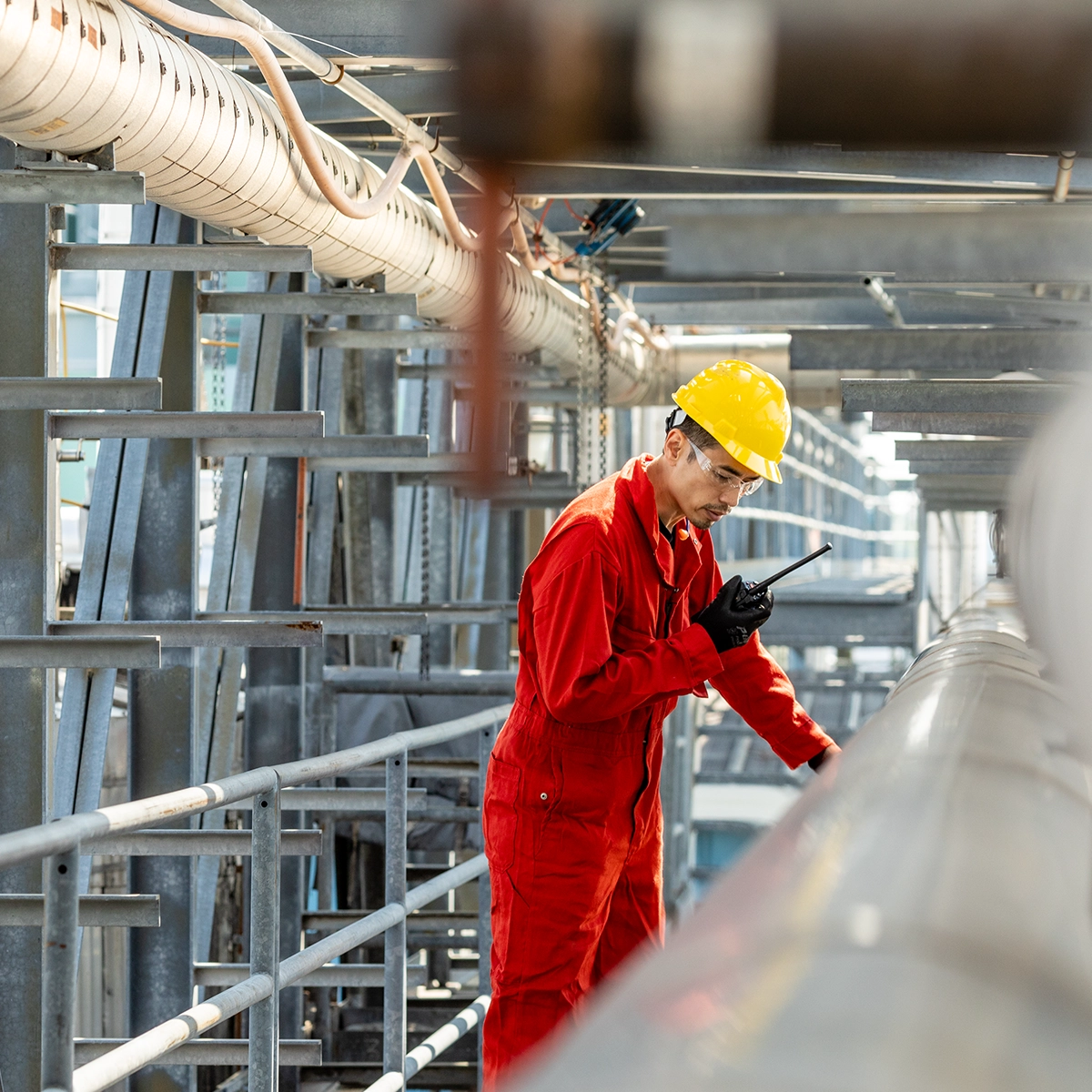 Lone worker operating a communication device while inspecting industrial infrastructure within a metal framework.