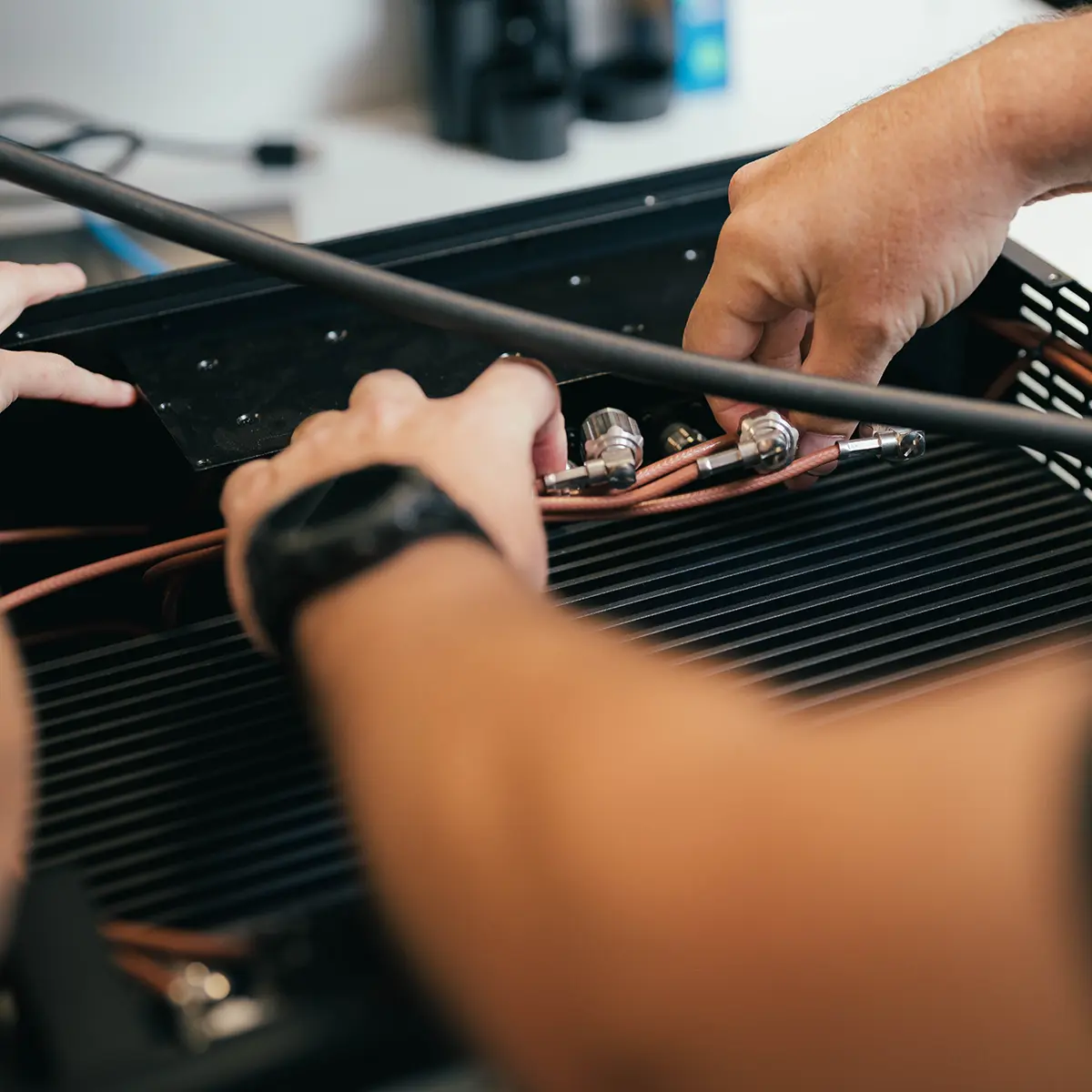 Hands performing maintenance on equipment, adjusting cables or pipes with a tool to ensure reliable operation