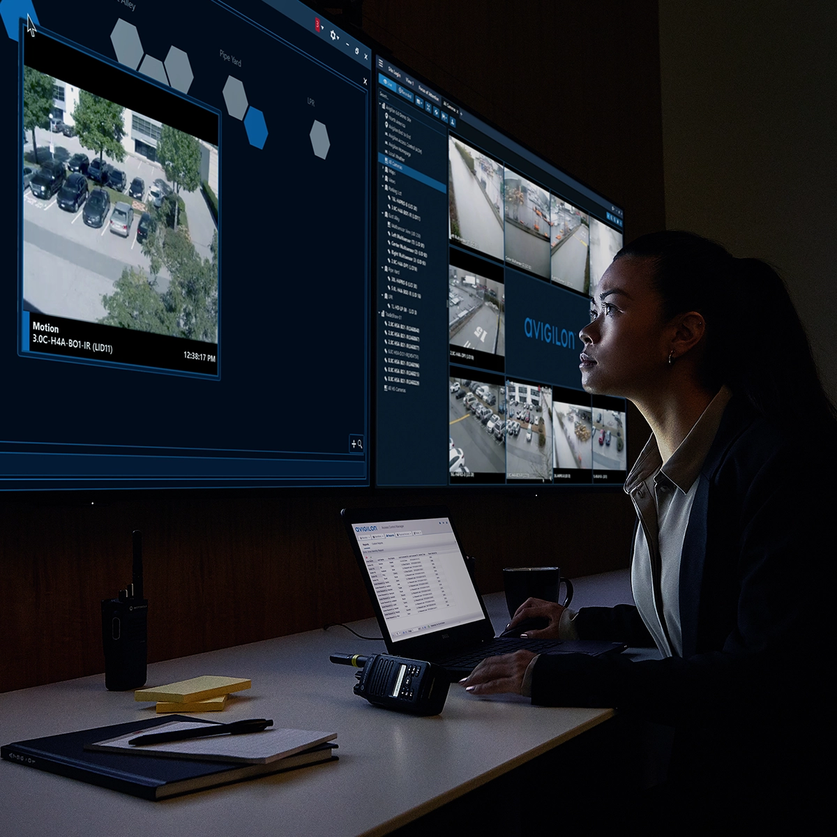 Security operator monitoring multiple camera feeds and software interfaces using Avigilon Alta Aware and Alta Control Center.