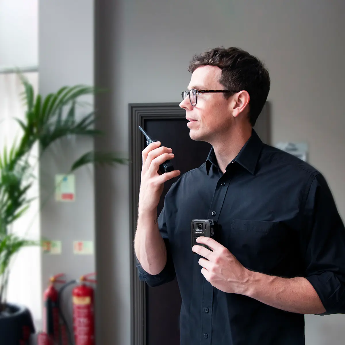 Technician calling for backup via radio and engaging a body-worn camera linked to a control room through an integrated communication network.