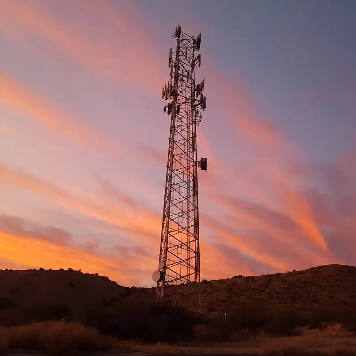 Tall communications tower silhouetted against a colourful sky in a remote Australian environment.