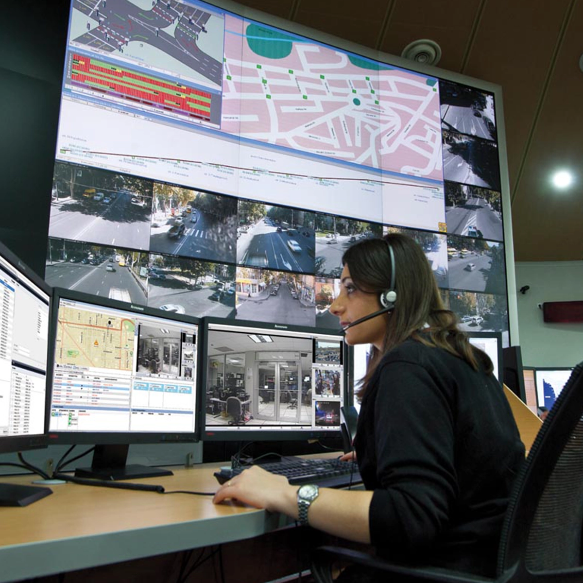 Security operator at a control desk monitoring surveillance feeds and maps using Avigilon analytics software.