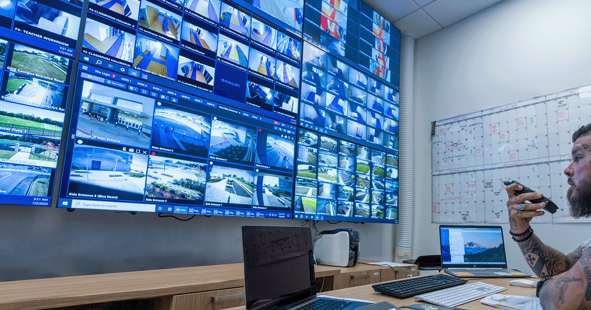 University Security Guard watches a wall of CCTV screens in a centralised control room.