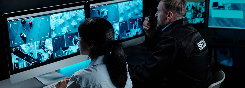 Security personnel monitoring data centre surveillance feeds in a control room.