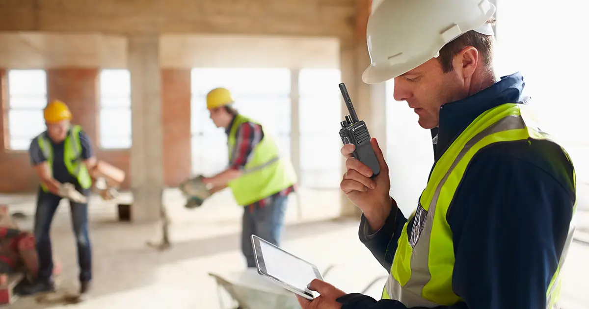 Construction worker in full PPE uses a Motorola Solutions DP4000e two-way radio on the Capacity Max network system to contact other team members.
