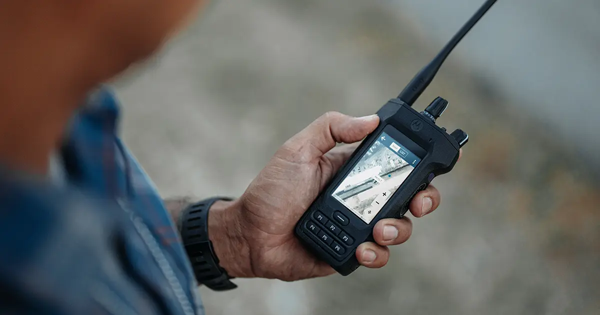 Close-up of a hand holding a Motorola Solutions two-way radio displaying a map, representing critical communication tools for campus emergency response.