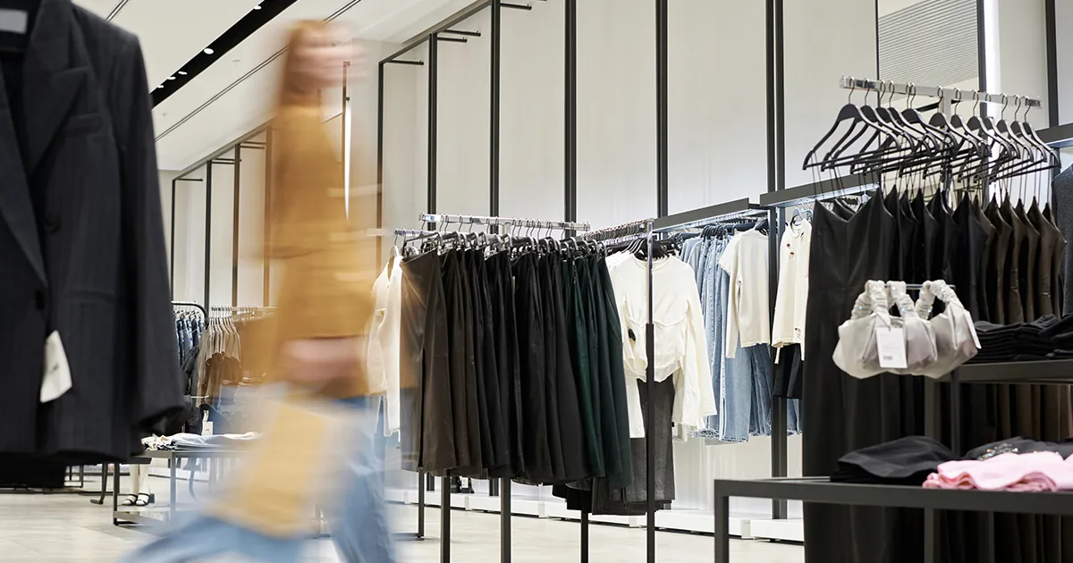 Contemporary fashion retail space with clothing racks and a customer walking past, illustrating environments where CSE Crosscom two-way radios enhance communication and operational efficiency.