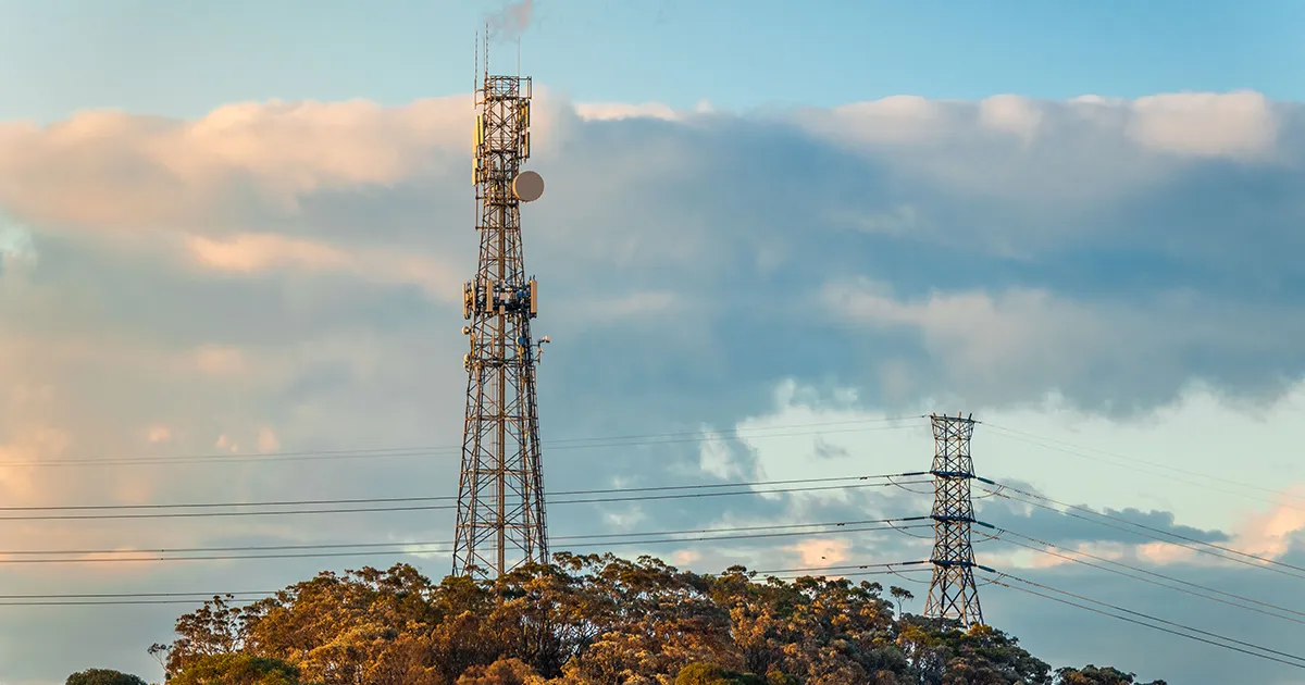 Mobile and radio tower rises above an Australian bush landscape at sunset with a transmission powerline in the background