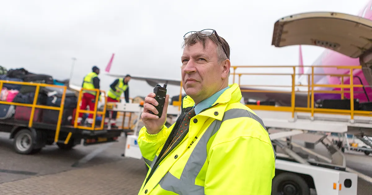 Airport baggage handler uses the Motorola Solutions MOTOTRBO Ion two-way radio to communicate while loading a commercial airplane with passenger luggage