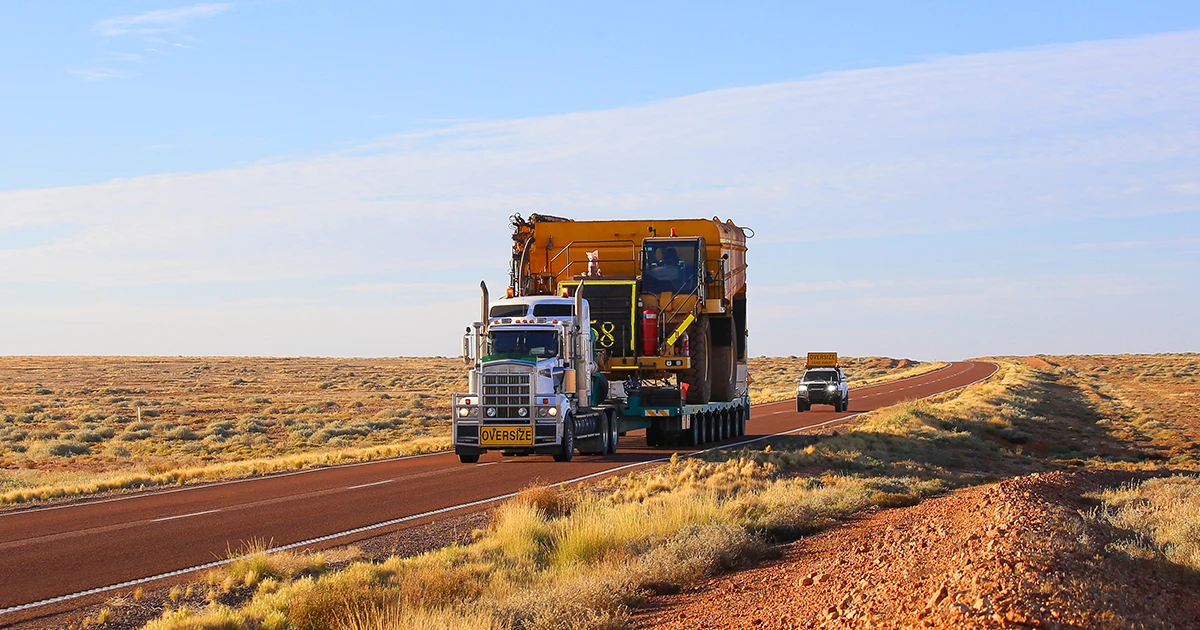 Road Train with oversized load drives along a remote Australian highway with a traffic management vehicle behind