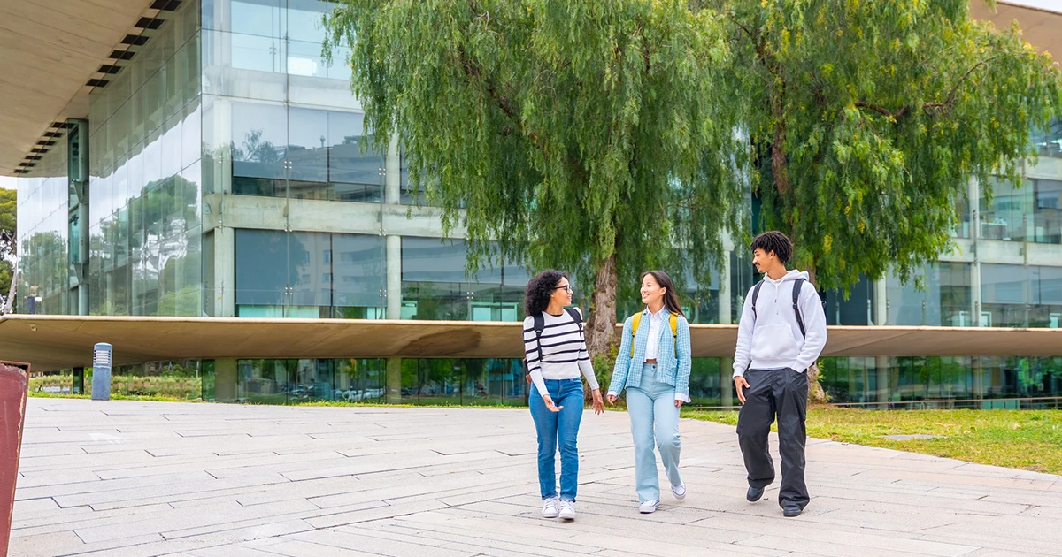 Three Australian university students walk past the outside of a University lecture hall