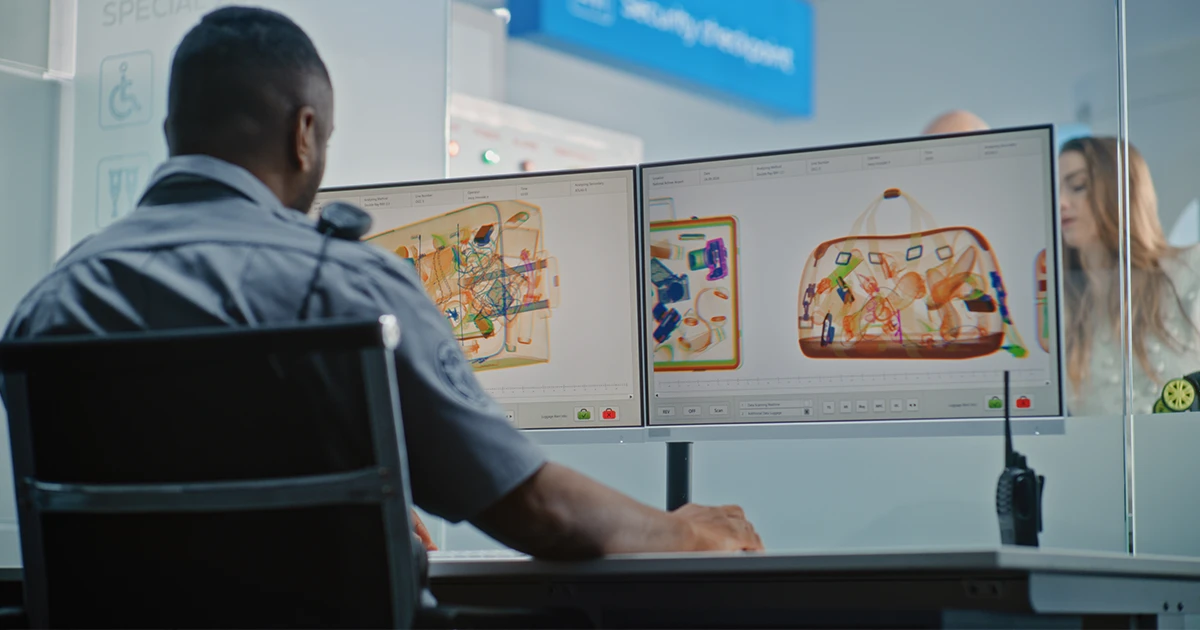 Security staff monitor the live results from the baggage x-ray conveyor belt in the security screening area of a busy airport