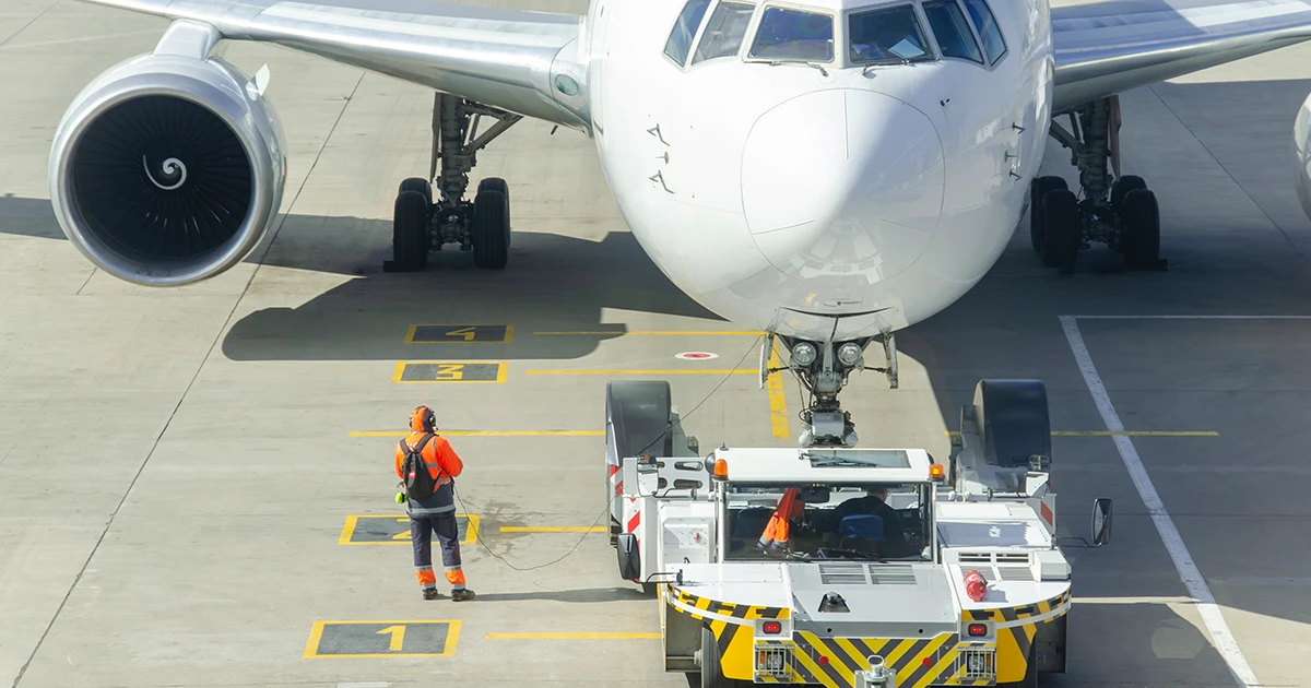 Ground air support staff uses a two way radio to communicate with airport staff while directing an aircraft on a tarmac