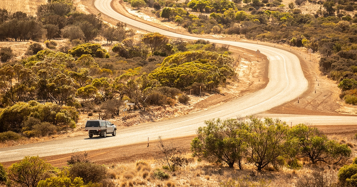 Contractor drives their mine-spec vehicle on a gravel dirt road towards an open pit mine in Australia's outback.
